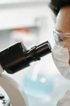 Scientist wearing protective glasses and a face mask while observing through a microscope in a laboratory