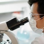 Scientist wearing protective glasses and a face mask while observing through a microscope in a laboratory